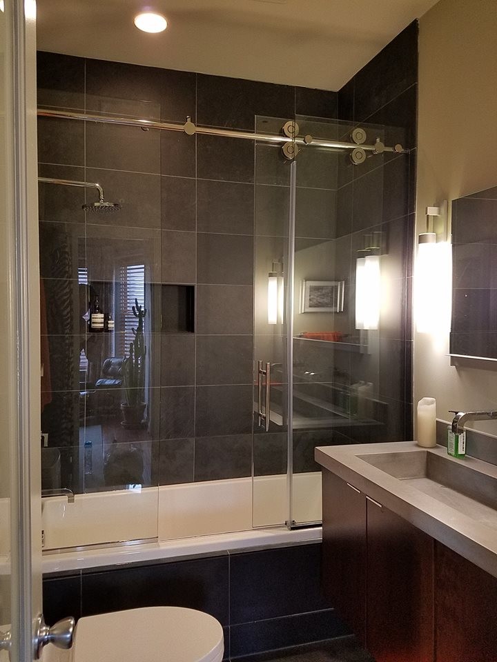 This is an example of a mid-sized contemporary 3/4 bathroom in Baltimore with flat-panel cabinets, dark wood cabinets, an alcove tub, a shower/bathtub combo, a one-piece toilet, black tile, slate, beige walls, slate floors, an integrated sink, concrete benchtops, black floor and a sliding shower screen.
