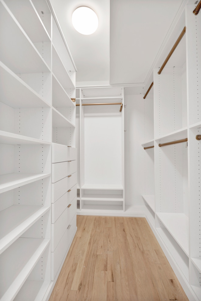 Photo of a large transitional gender-neutral walk-in wardrobe in New York with open cabinets, white cabinets, light hardwood floors and beige floor.