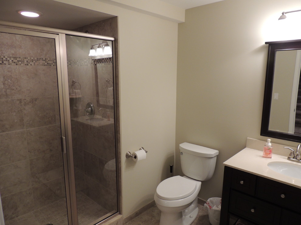 Design ideas for a mid-sized traditional 3/4 bathroom in Detroit with flat-panel cabinets, dark wood cabinets, an alcove shower, a one-piece toilet, beige tile, stone tile, beige walls, limestone floors, an undermount sink and engineered quartz benchtops.