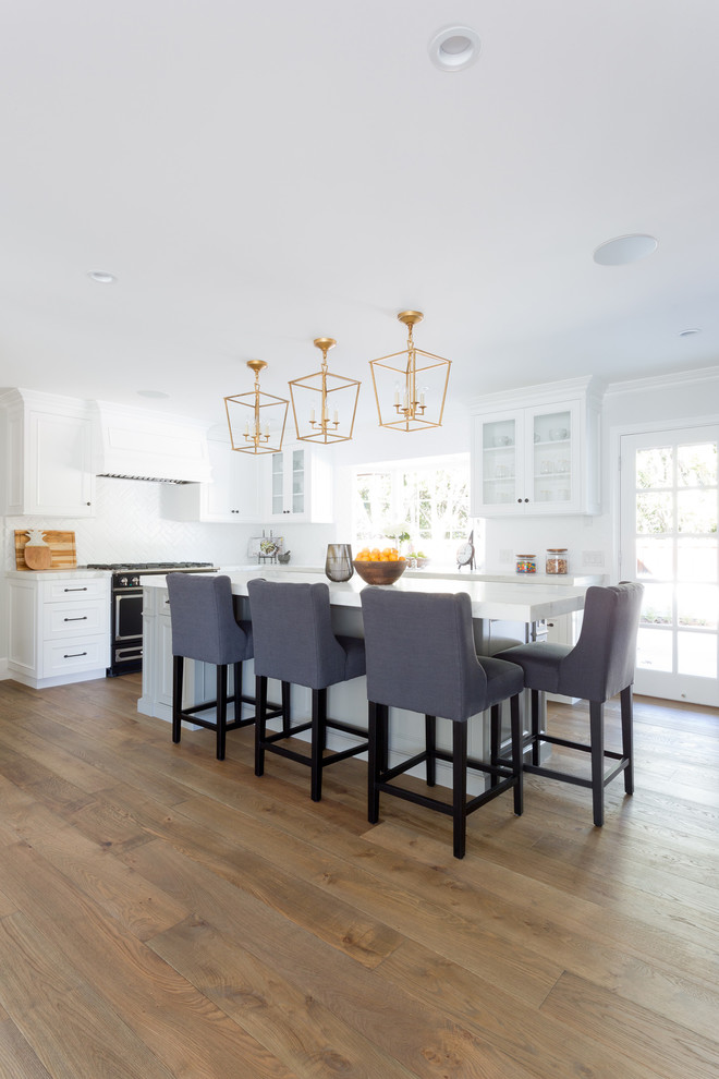 Large transitional l-shaped light wood floor open concept kitchen photo in Orange County with a farmhouse sink, shaker cabinets, white cabinets, marble countertops, white backsplash, brick backsplash, stainless steel appliances and an island