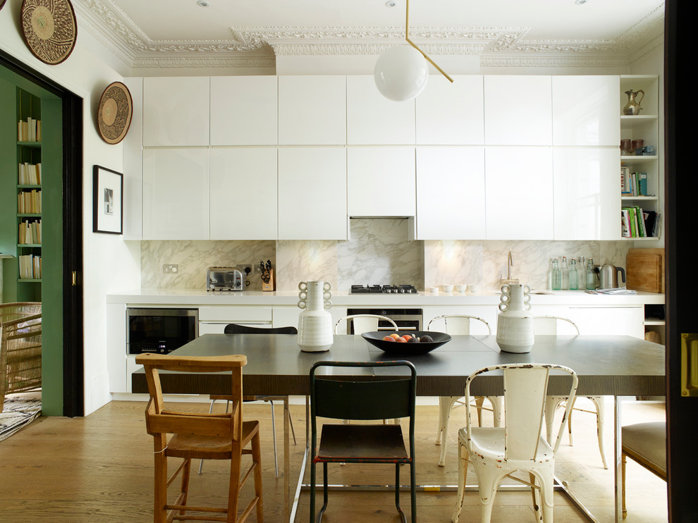 This is an example of an eclectic single-wall eat-in kitchen in London with flat-panel cabinets, white cabinets, white splashback, stone slab splashback, stainless steel appliances, medium hardwood floors and no island.