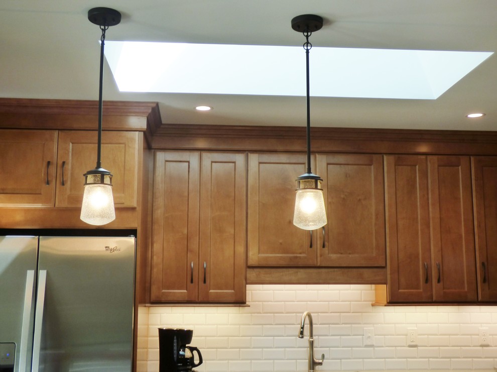Inspiration for a transitional l-shaped porcelain tile eat-in kitchen remodel with an undermount sink, recessed-panel cabinets, medium tone wood cabinets, quartz countertops, white backsplash, subway tile backsplash, stainless steel appliances and an island