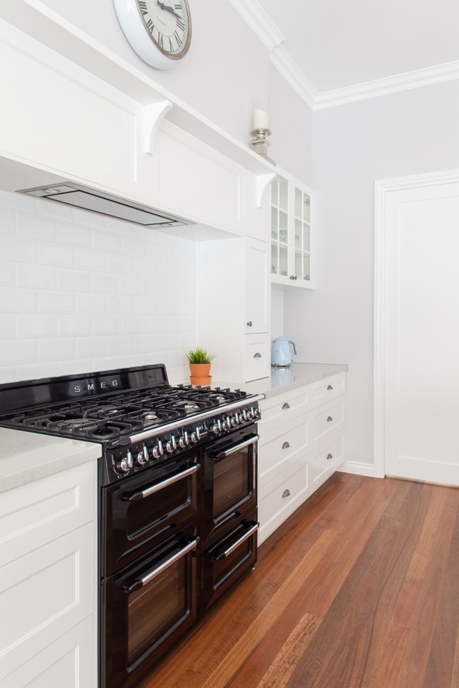 This is an example of a traditional kitchen in Brisbane with an undermount sink, glass-front cabinets, white cabinets, black appliances, dark hardwood floors and with island.