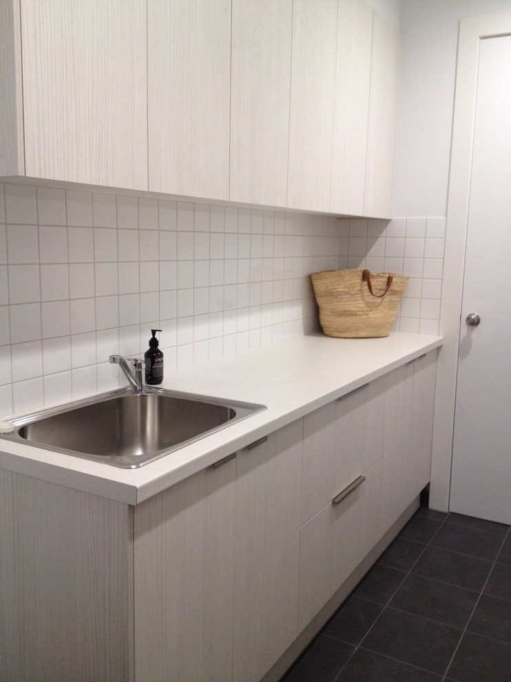 Inspiration for a large contemporary galley dedicated laundry room in Melbourne with a single-bowl sink, flat-panel cabinets, light wood cabinets, laminate benchtops, white walls, porcelain floors and a stacked washer and dryer.