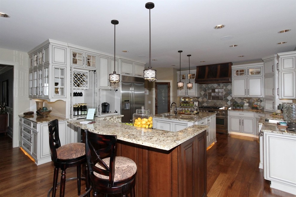 Example of a large transitional u-shaped medium tone wood floor kitchen pantry design in Chicago with beige backsplash, ceramic backsplash, two islands, a double-bowl sink, raised-panel cabinets, distressed cabinets, granite countertops and stainless steel appliances