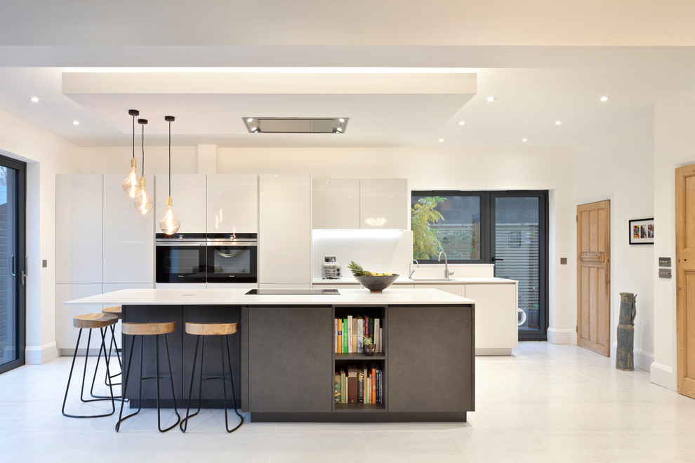 Photo of a mid-sized eclectic single-wall open plan kitchen in London with an integrated sink, flat-panel cabinets, grey cabinets, quartzite benchtops, grey splashback, stone slab splashback, black appliances, porcelain floors, with island, grey floor and grey benchtop.