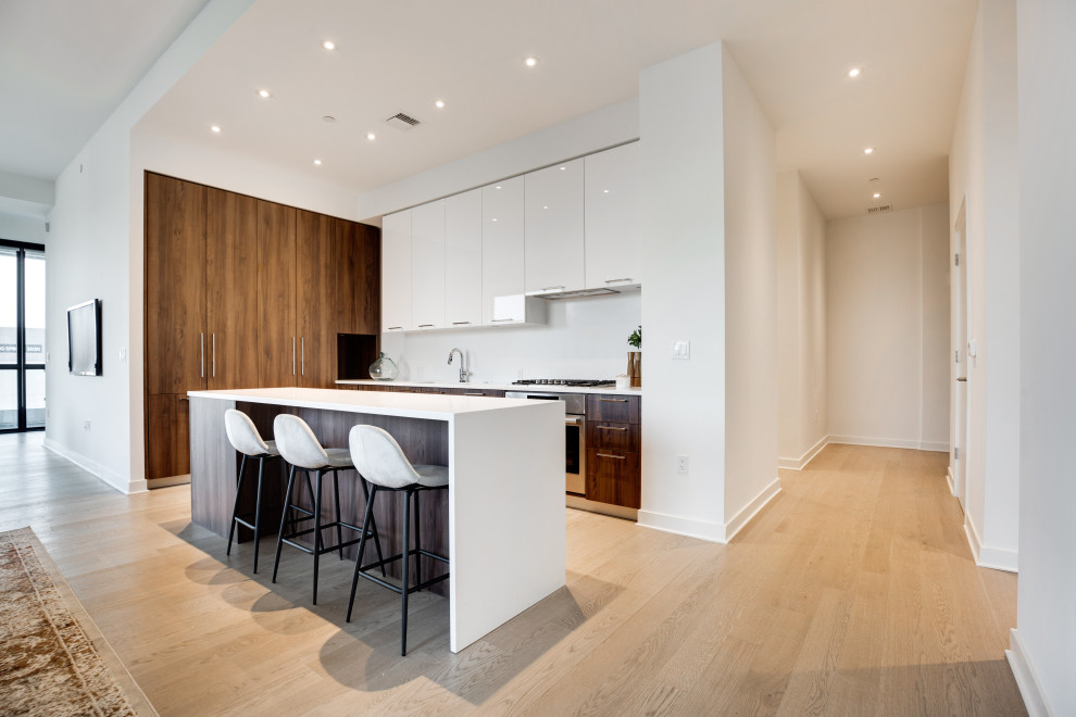 Inspiration for a mid-sized modern l-shaped eat-in kitchen in DC Metro with flat-panel cabinets, white cabinets, quartz benchtops, light hardwood floors, with island, brown floor and white benchtop.