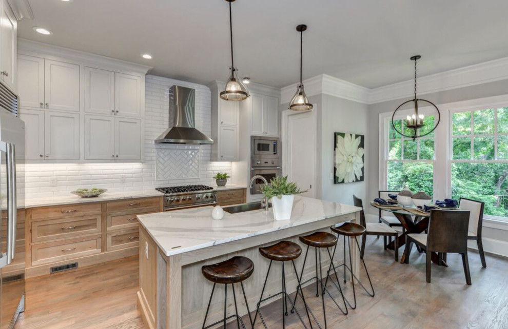 Inspiration for a large transitional l-shaped light wood floor and beige floor enclosed kitchen remodel in Atlanta with a farmhouse sink, beaded inset cabinets, white backsplash, ceramic backsplash, stainless steel appliances, an island, light wood cabinets and marble countertops