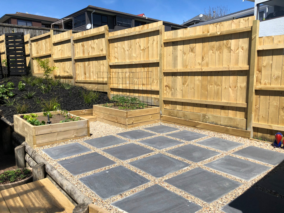Photo of a small tropical backyard formal garden for spring in Auckland with with raised garden bed, mulch and a wood fence.