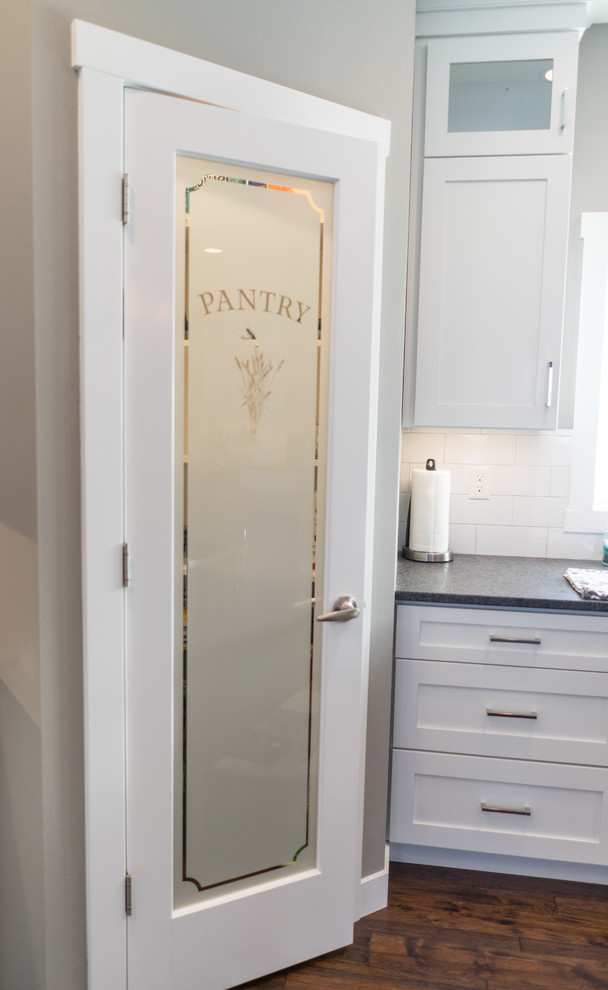 Example of a large transitional u-shaped eat-in kitchen design with a farmhouse sink, flat-panel cabinets, white cabinets, granite countertops, white backsplash, ceramic backsplash, stainless steel appliances and an island