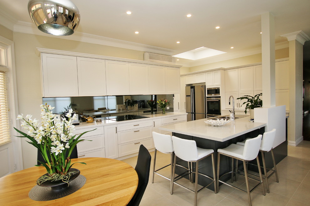 Large transitional l-shaped eat-in kitchen in Sydney with a drop-in sink, shaker cabinets, white cabinets, quartz benchtops, grey splashback, glass sheet splashback, stainless steel appliances, ceramic floors and with island.