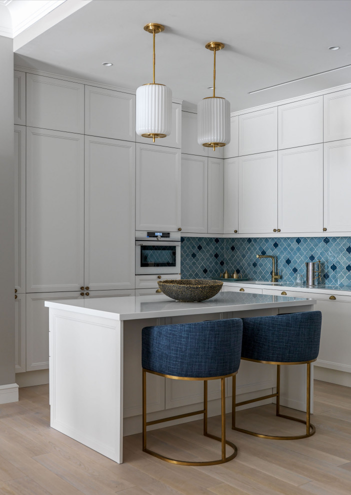 Photo of a mid-sized transitional l-shaped kitchen in Moscow with an integrated sink, shaker cabinets, white cabinets, blue splashback, porcelain splashback, panelled appliances, light hardwood floors, with island, beige floor and white benchtop.