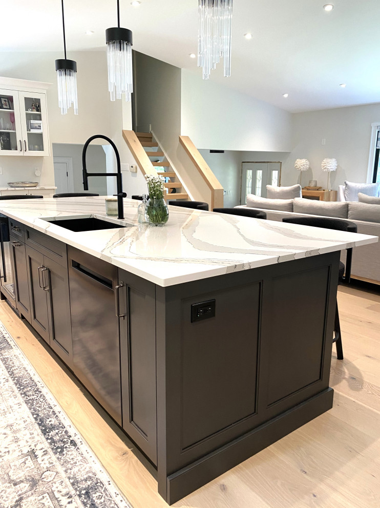 Large transitional l-shaped light wood floor and vaulted ceiling open concept kitchen photo in Toronto with an undermount sink, recessed-panel cabinets, white cabinets, quartz countertops, white backsplash, porcelain backsplash, stainless steel appliances, an island and white countertops