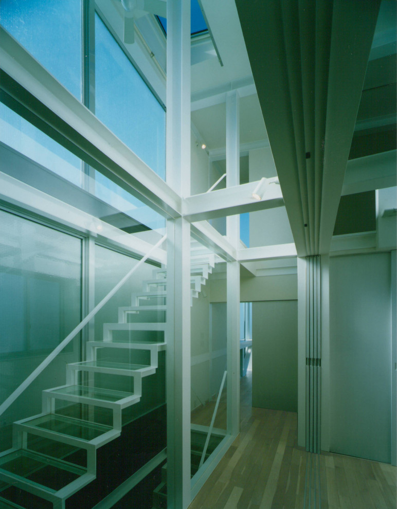 Cette image montre un escalier flottant urbain de taille moyenne avec des marches en verre, des contremarches en verre et un garde-corps en métal.