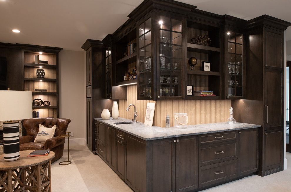 Design ideas for a mid-sized transitional l-shaped wet bar in Minneapolis with an undermount sink, glass-front cabinets, dark wood cabinets, marble benchtops, beige splashback, timber splashback, carpet, beige floor and grey benchtop.