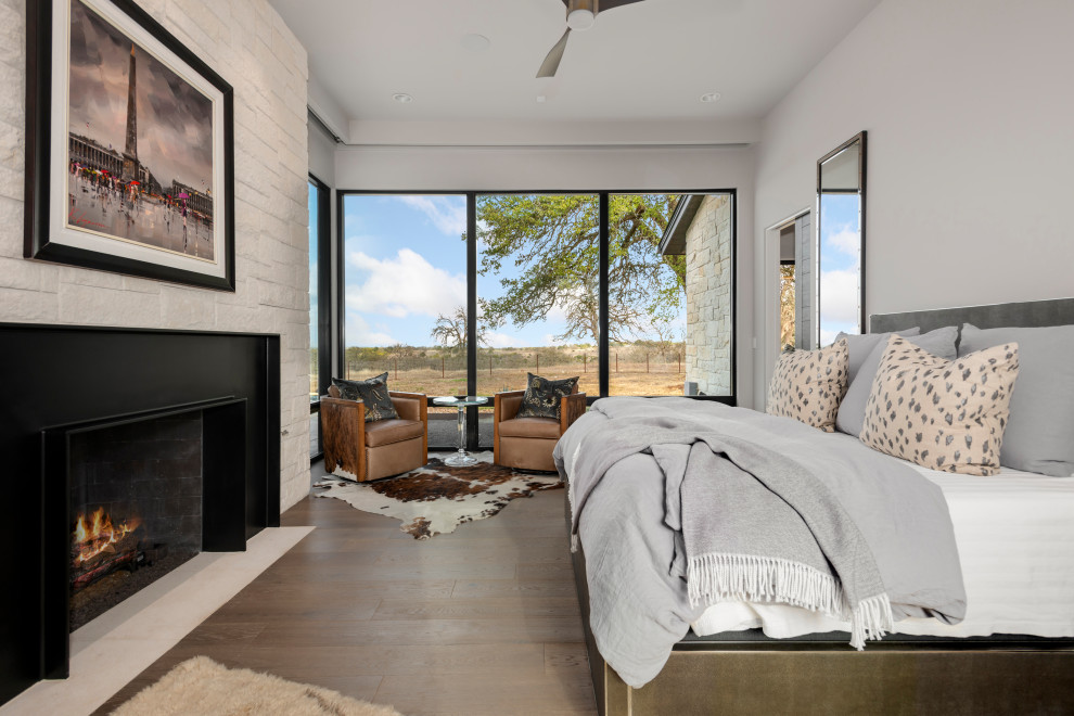 Contemporary bedroom in Austin with grey walls, dark hardwood floors, a standard fireplace and brown floor.