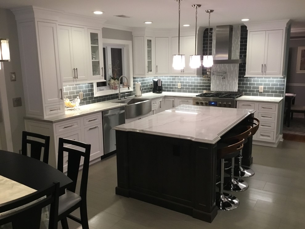 Mid-sized transitional l-shaped porcelain tile and gray floor kitchen photo in New York with a farmhouse sink, beaded inset cabinets, white cabinets, quartzite countertops, gray backsplash, subway tile backsplash, stainless steel appliances, an island and white countertops