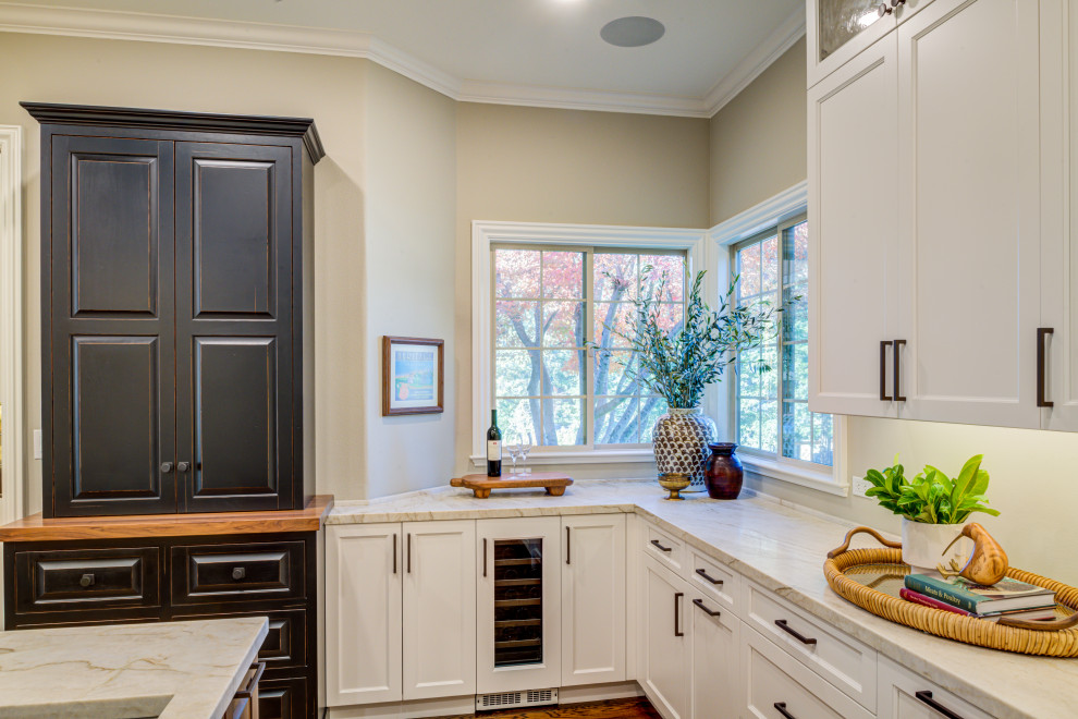 Cette photo montre une cuisine américaine chic en L de taille moyenne avec un placard à porte affleurante, des portes de placard noires, un plan de travail en quartz, îlot, un sol marron et un plan de travail beige.
