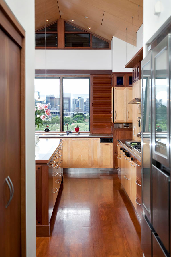 Photo of an expansive transitional l-shaped kitchen in Brisbane with a double-bowl sink, flat-panel cabinets, stainless steel benchtops, stainless steel appliances, medium hardwood floors, with island and brown floor.