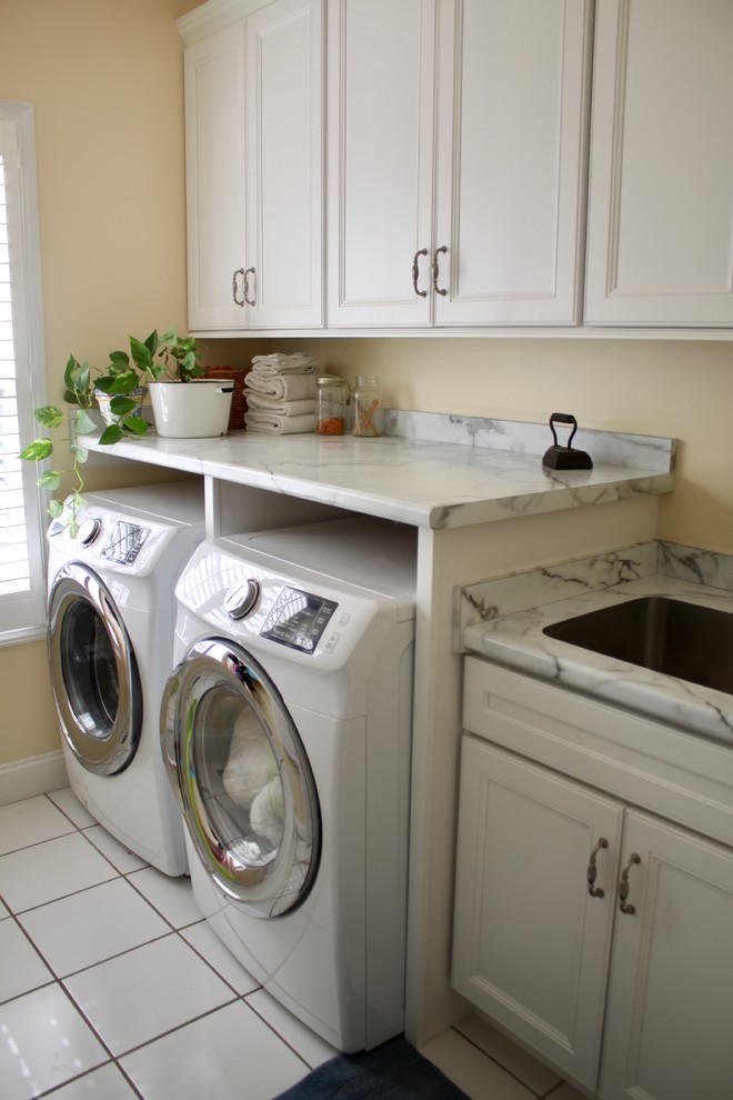 Inspiration for a mid-sized transitional galley utility room in Other with an undermount sink, white cabinets, beige walls, a side-by-side washer and dryer, white floor, recessed-panel cabinets, ceramic floors and grey benchtop.