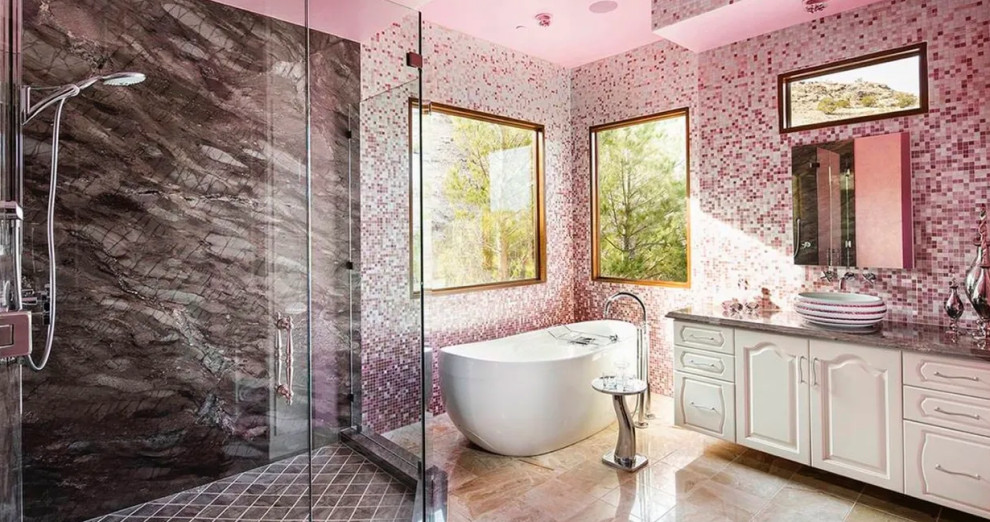 Photo of a large eclectic master bathroom in Las Vegas with raised-panel cabinets, white cabinets, a freestanding tub, a corner shower, pink tile, mosaic tile, a vessel sink, beige floor, a hinged shower door and grey benchtops.