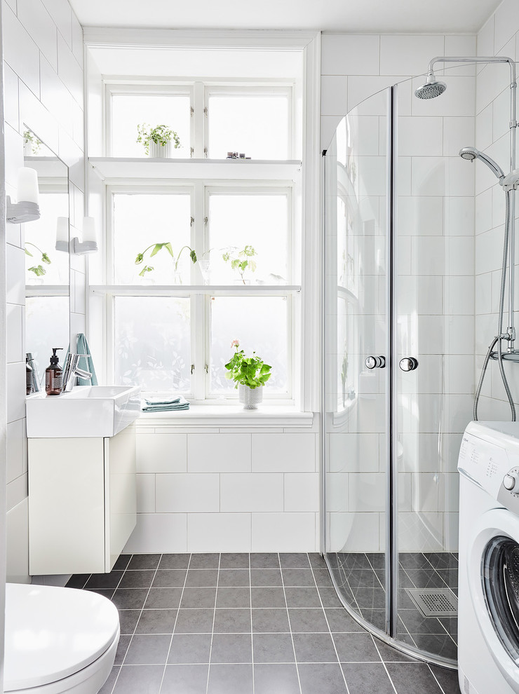Inspiration for a mid-sized scandinavian bathroom in Gothenburg with flat-panel cabinets, white cabinets, a corner shower, gray tile, white tile, ceramic tile, limestone floors, an undermount sink, a hinged shower door and a laundry.