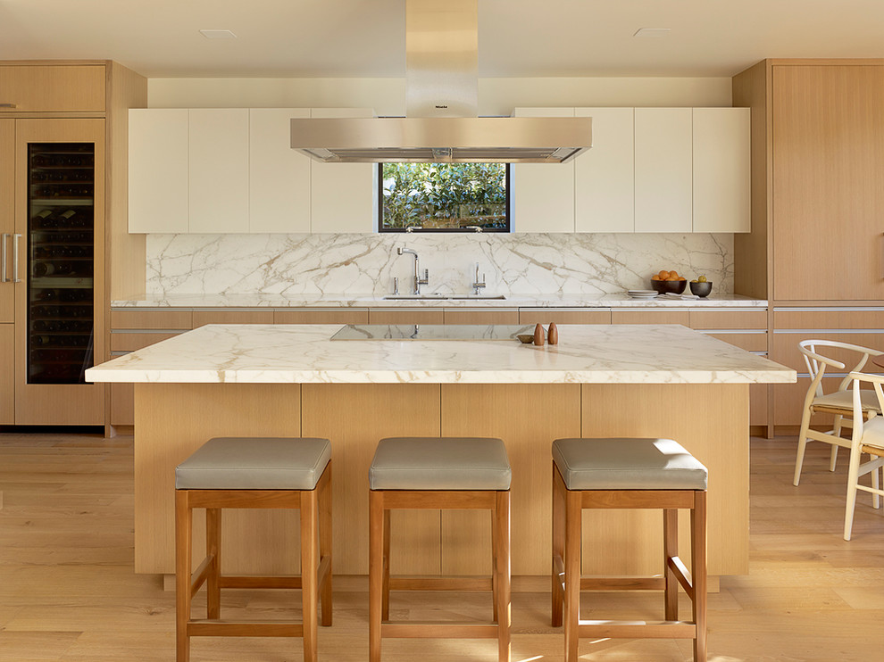This is an example of a midcentury eat-in kitchen in San Francisco with an undermount sink, flat-panel cabinets, light wood cabinets, marble benchtops, white splashback, stone slab splashback, panelled appliances, light hardwood floors and with island.