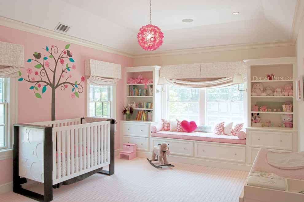 This is an example of a large transitional nursery for girls in New York with pink walls, carpet and beige floor.