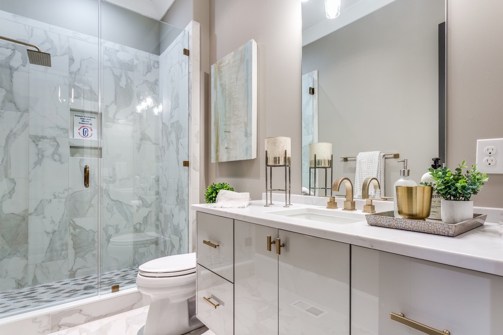 Inspiration for a transitional 3/4 gray tile and white tile gray floor alcove shower remodel with flat-panel cabinets, gray cabinets, a two-piece toilet, beige walls, an undermount sink, a hinged shower door and white countertops