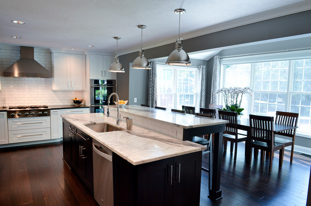 Eat-in kitchen - transitional dark wood floor eat-in kitchen idea in Cleveland with a drop-in sink, recessed-panel cabinets, white backsplash, ceramic backsplash, stainless steel appliances and an island