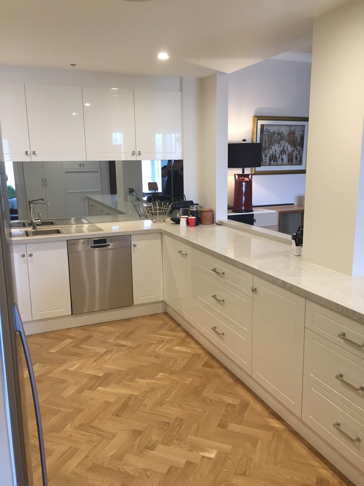 Mid-sized traditional u-shaped open plan kitchen in Melbourne with a double-bowl sink, shaker cabinets, white cabinets, quartz benchtops, metallic splashback, mirror splashback, stainless steel appliances and medium hardwood floors.