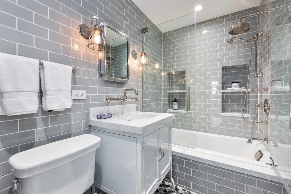 This is an example of a small industrial master bathroom in Chicago with white cabinets, a drop-in tub, a two-piece toilet, gray tile, ceramic tile, grey walls, ceramic floors, an undermount sink and marble benchtops.