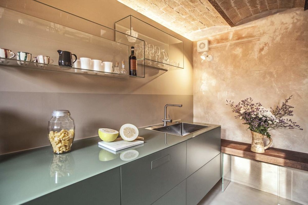 Photo of an industrial kitchen in Venice with a single-bowl sink, flat-panel cabinets, grey cabinets, concrete floors, grey floor, glass benchtops, grey splashback and grey benchtop.