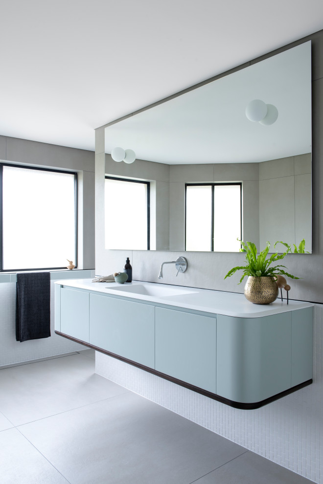 Large contemporary bathroom in Sydney with blue cabinets, mosaic tile, porcelain floors, an integrated sink, solid surface benchtops, grey floor, white benchtops, flat-panel cabinets and white tile.