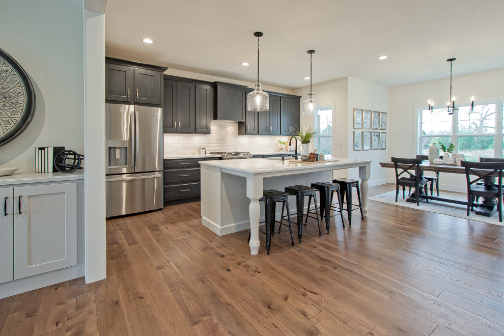 Example of a transitional single-wall light wood floor and brown floor eat-in kitchen design with an undermount sink, raised-panel cabinets, dark wood cabinets, quartz countertops, white backsplash, brick backsplash, stainless steel appliances, an island and white countertops