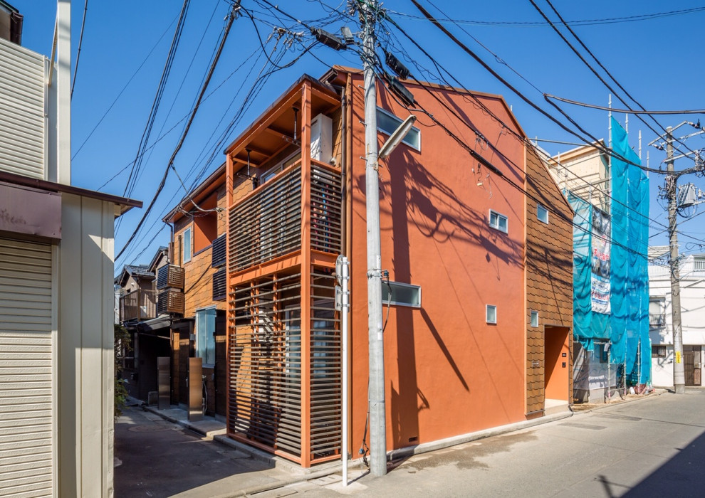 This is an example of a mid-sized scandinavian two-storey orange house exterior in Tokyo with painted brick siding, a gable roof and a shingle roof.