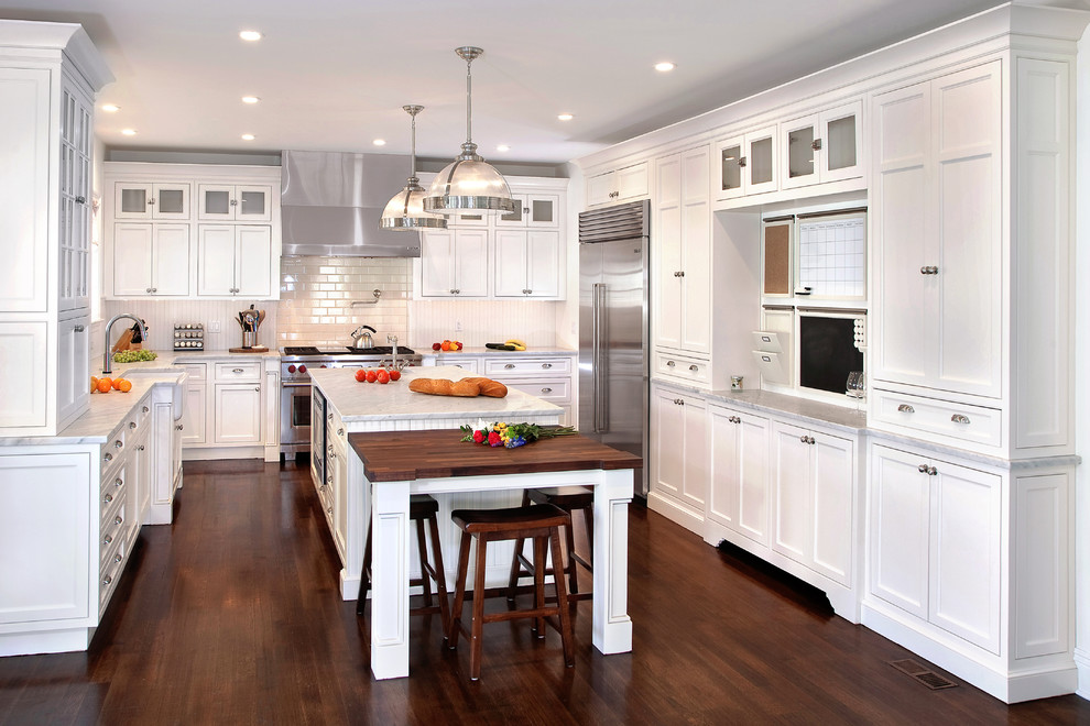 Elegant u-shaped dark wood floor kitchen photo in Dallas with a farmhouse sink, recessed-panel cabinets, white cabinets, white backsplash, subway tile backsplash, stainless steel appliances and an island