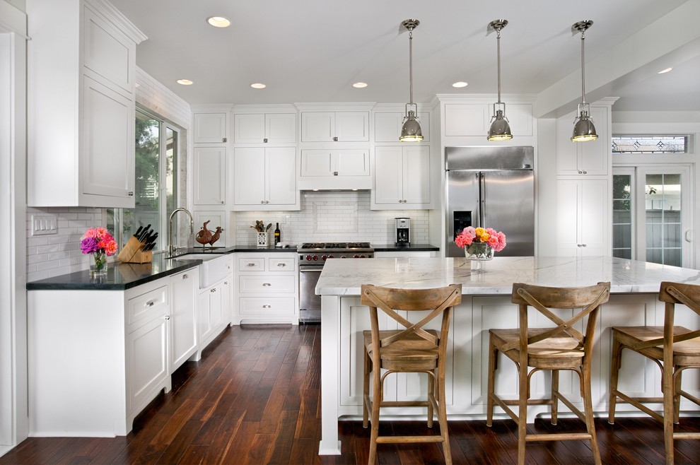Example of a classic l-shaped eat-in kitchen design in San Diego with a farmhouse sink, shaker cabinets, white cabinets, soapstone countertops, white backsplash, subway tile backsplash and stainless steel appliances