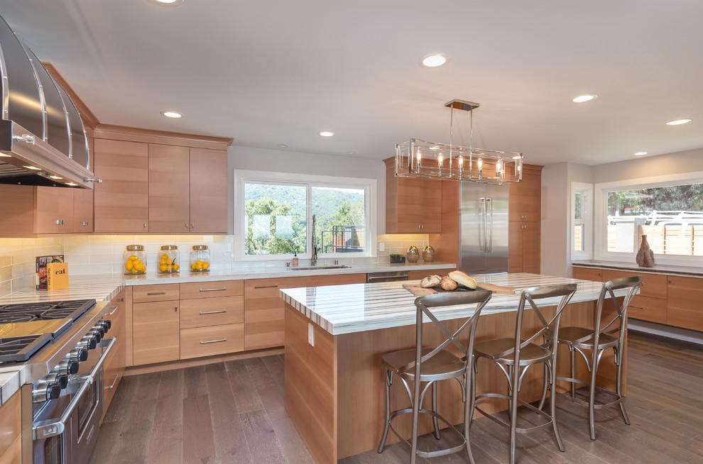 This is an example of a contemporary kitchen in San Francisco with an undermount sink, flat-panel cabinets, light wood cabinets, white splashback, stainless steel appliances, light hardwood floors and with island.