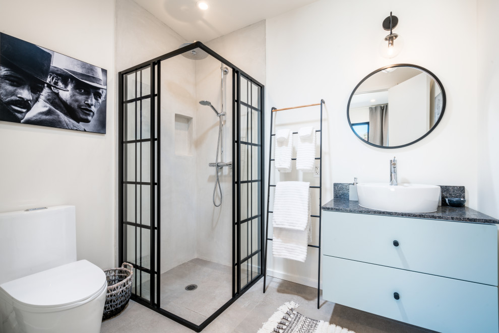 Inspiration for a mid-sized industrial 3/4 bathroom in Other with flat-panel cabinets, blue cabinets, a corner shower, white walls, a vessel sink, grey floor, grey benchtops, a two-piece toilet, concrete floors, soapstone benchtops and a sliding shower screen.