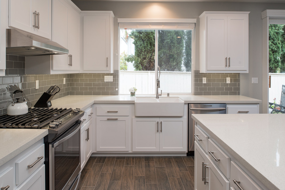Mid-sized modern u-shaped kitchen in San Diego with a farmhouse sink, shaker cabinets, white cabinets, quartz benchtops, grey splashback, subway tile splashback, stainless steel appliances, plywood floors and with island.