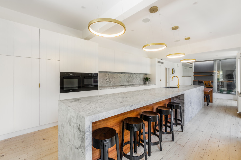 Inspiration for a large contemporary galley eat-in kitchen in Melbourne with an undermount sink, white cabinets, marble benchtops, grey splashback, marble splashback, black appliances, light hardwood floors, with island and grey benchtop.