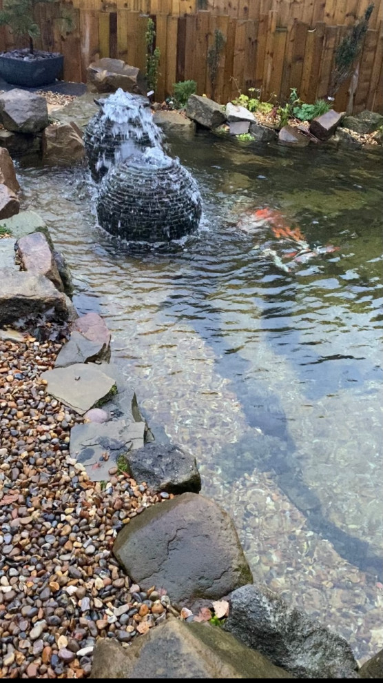This is an example of a farmhouse back formal partial sun garden for summer in Manchester with a waterfall, decorative stones and a wood fence.