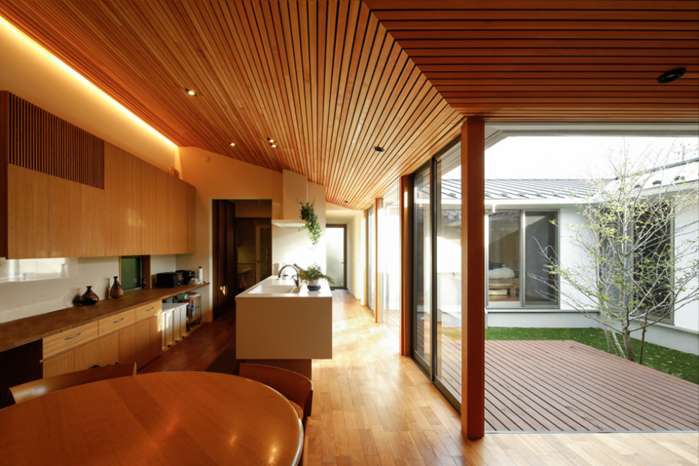This is an example of a medium sized single-wall open plan kitchen in Yokohama with an integrated sink, flat-panel cabinets, white cabinets, composite countertops, white splashback, stainless steel appliances, dark hardwood flooring, a breakfast bar, brown floors, white worktops and a wood ceiling.