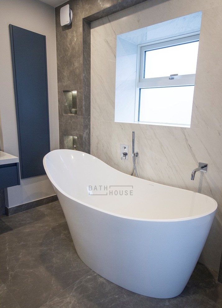 Photo of a mid-sized contemporary master wet room bathroom in Dublin with flat-panel cabinets, blue cabinets, a freestanding tub, a wall-mount toilet, multi-coloured tile, ceramic tile, white walls, porcelain floors, a vessel sink, tile benchtops, grey floor, an open shower and grey benchtops.