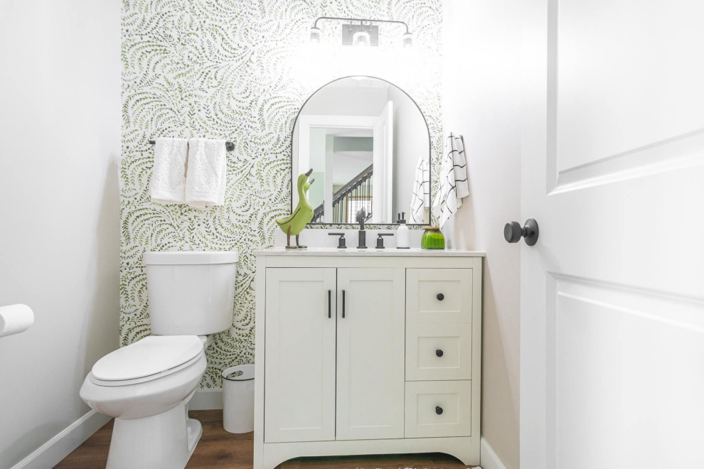 Photo of a small powder room in Minneapolis with shaker cabinets, white cabinets, a one-piece toilet, beige walls, laminate floors, marble benchtops, brown floor, white benchtops, a freestanding vanity and wallpaper.