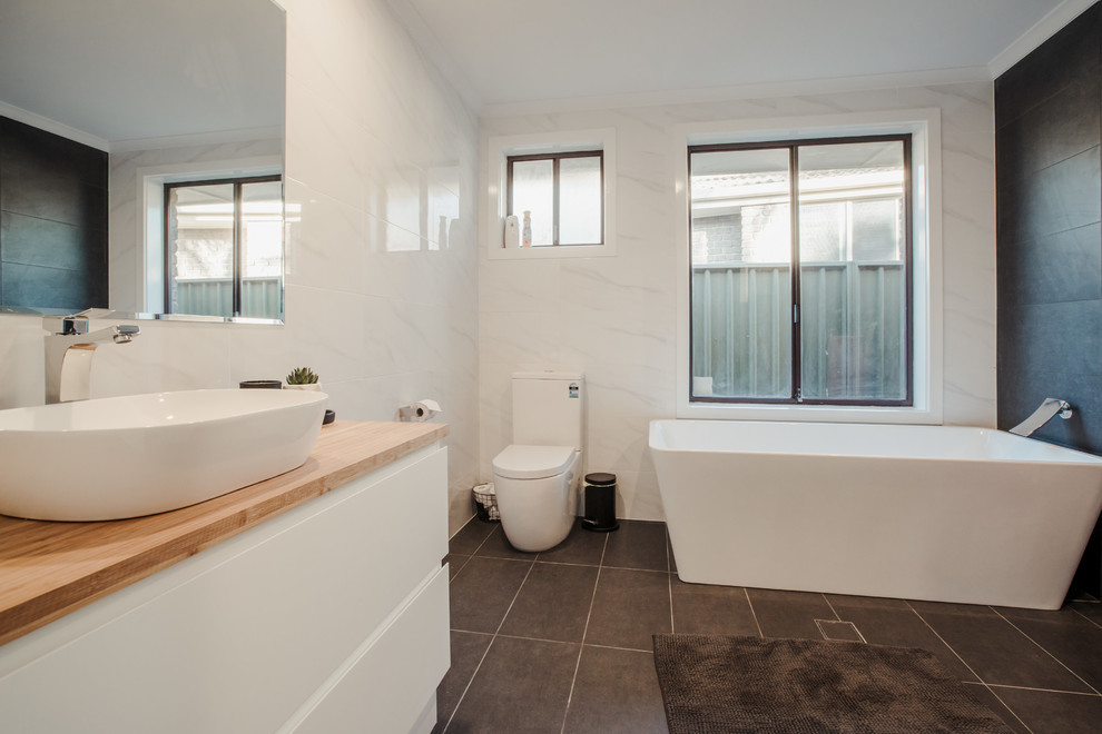 Design ideas for a mid-sized contemporary kids bathroom in Adelaide with flat-panel cabinets, white cabinets, a freestanding tub, a corner shower, a two-piece toilet, white tile, ceramic tile, white walls, ceramic floors, a vessel sink, wood benchtops, grey floor and a hinged shower door.