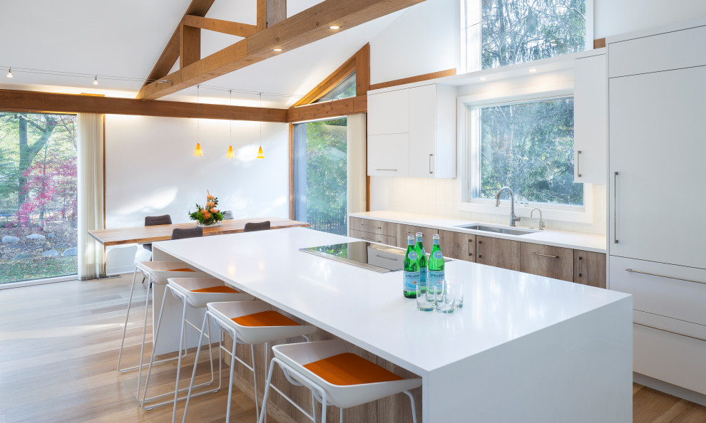 Photo of a large contemporary eat-in kitchen in Grand Rapids with an undermount sink, flat-panel cabinets, light wood cabinets, quartz benchtops, white splashback, ceramic splashback, light hardwood floors, with island, white benchtop and exposed beam.