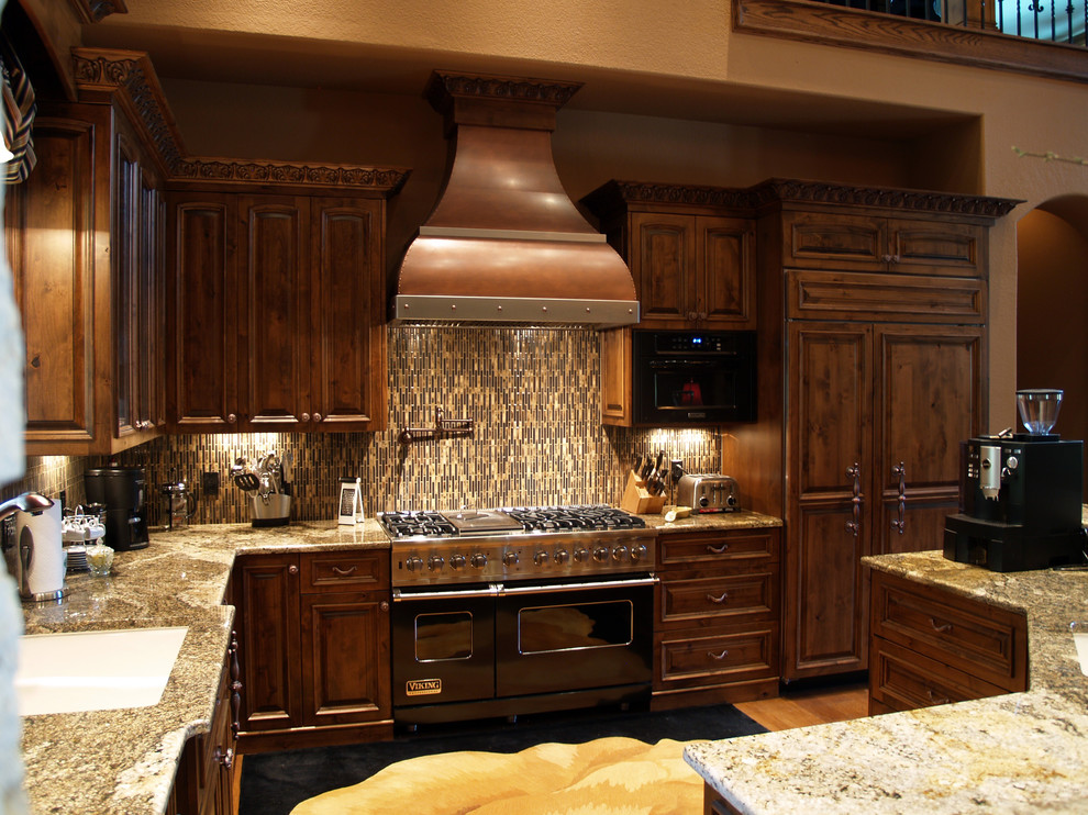 Inspiration for a transitional l-shaped medium tone wood floor open concept kitchen remodel in Austin with raised-panel cabinets, medium tone wood cabinets, granite countertops, multicolored backsplash, glass tile backsplash, paneled appliances and an island
