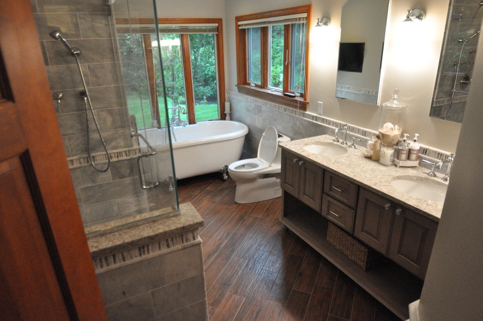 This is an example of a mid-sized traditional master bathroom in Boston with raised-panel cabinets, dark wood cabinets, a claw-foot tub, an alcove shower, a one-piece toilet, gray tile, beige walls, dark hardwood floors, an undermount sink, engineered quartz benchtops, brown floor and a hinged shower door.